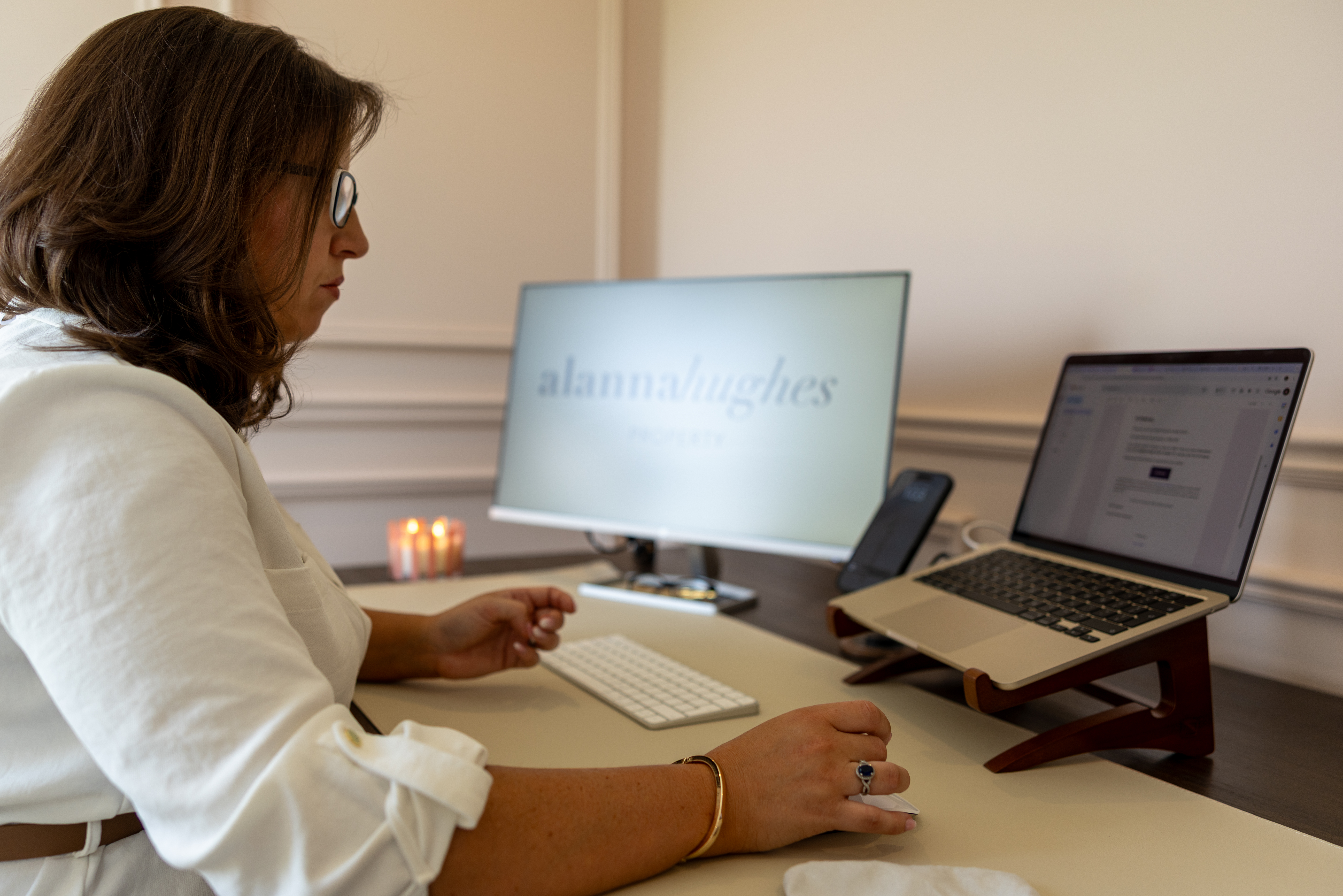 Alanna Hughes reviewing a client file at her desk, Alanna Hughes Property branding on screen